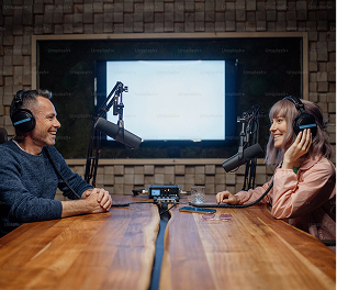 Man and woman with microphone and headphones sitting at a table conducting a podcast conversation