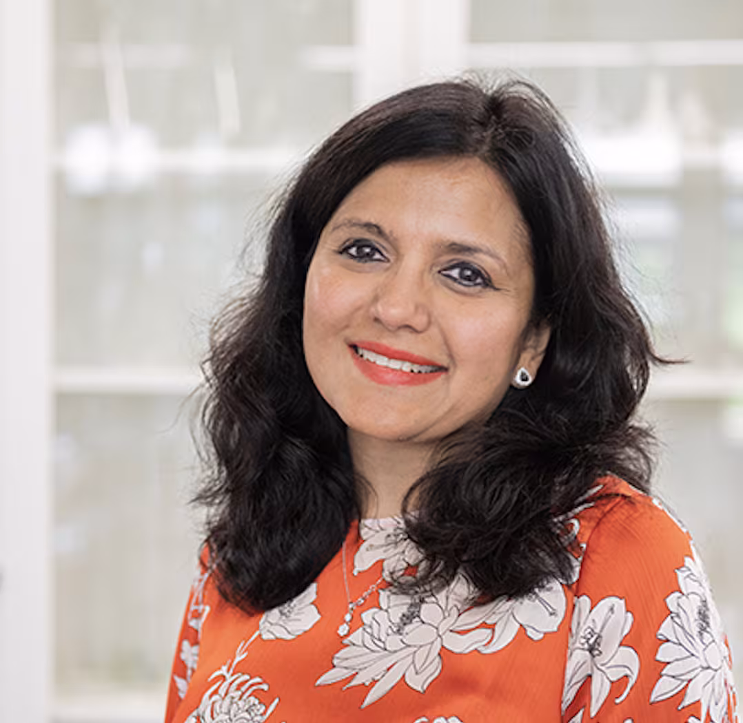 A portrait of Rohini Kuner. With her shoulder-length, dark brown hair, she smiles at the viewer and is wearing a red blouse with a white floral pattern. 